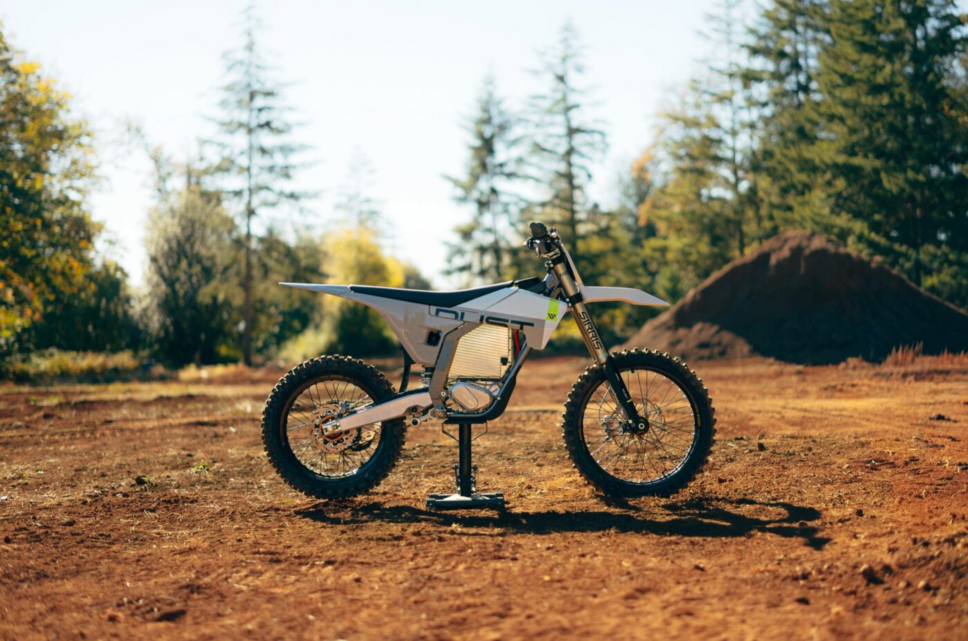 Dust Hightail Elektro-Motocrossmaschine in Weiß auf rotem Sandboden vor Waldkulisse