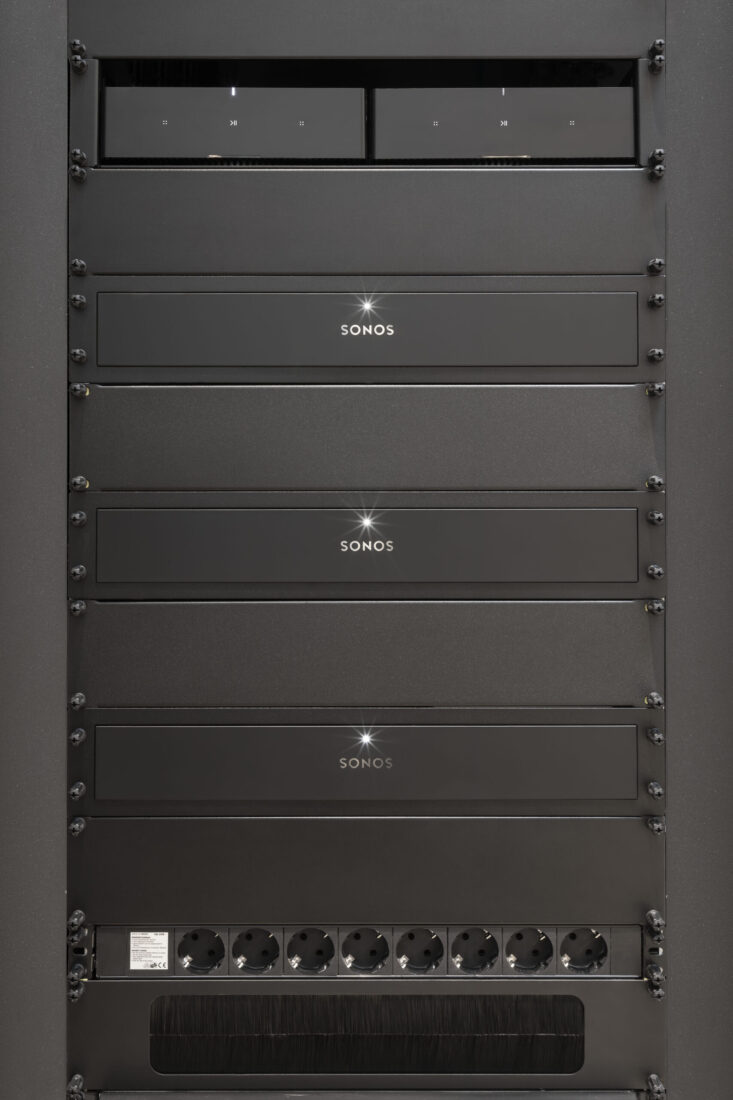 Drei Sonos Amp-Einheiten in einem schwarzen 19-Zoll-Rack mit Steckdosenleiste
