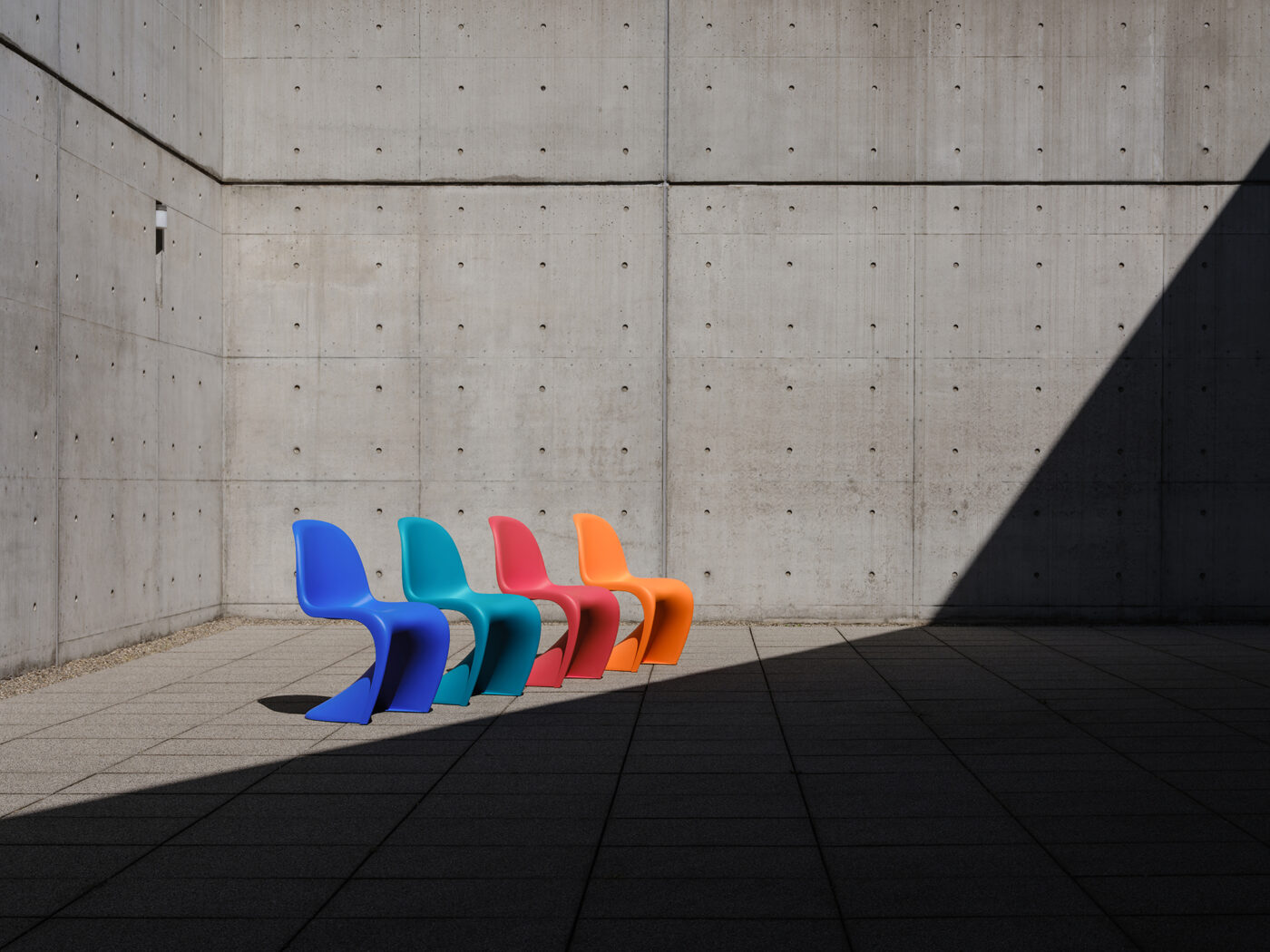 Vier Panton Chairs in Blau, Türkis, Rot und Orange vor Sichtbetonwand