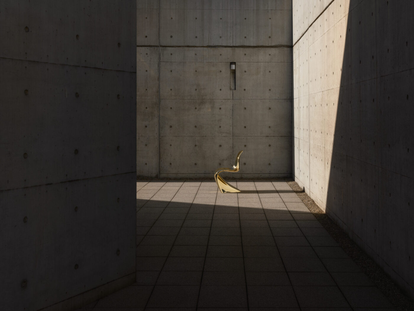 Goldener Panton Chair Classic Edition auf grauem Betonboden, beleuchtet von seitlichem Sonnenlicht