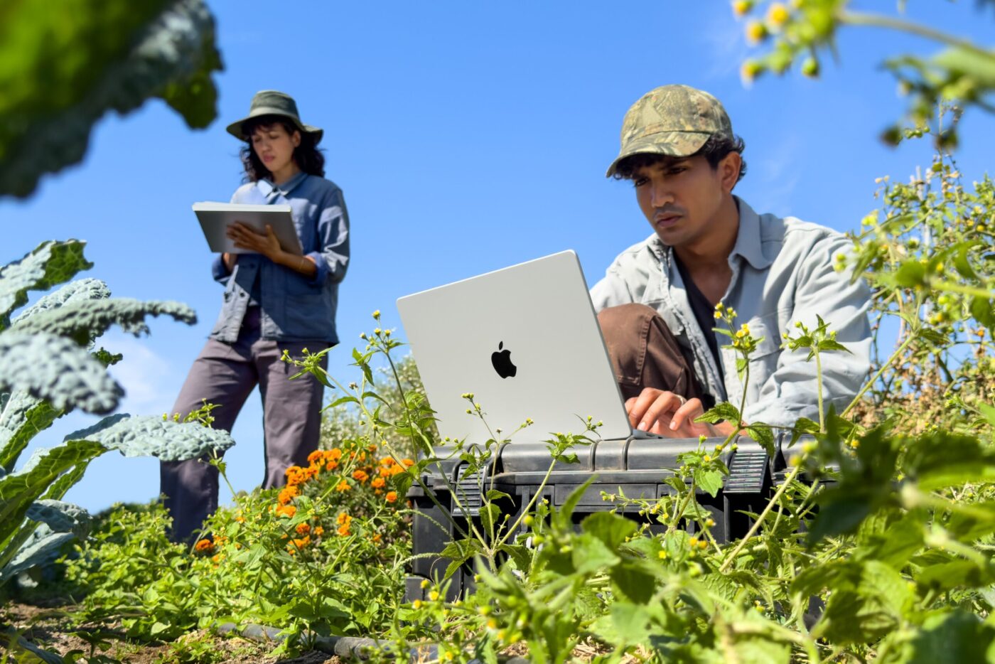 Mann tippt auf Apple MacBook Pro M6 auf Feld, Frau mit Tablet im Hintergrund