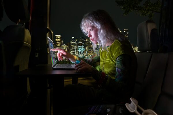 Frau bedient den Touchscreen eines Apple MacBook Pro nachts in einem Fahrzeug vor beleuchteter Skyline