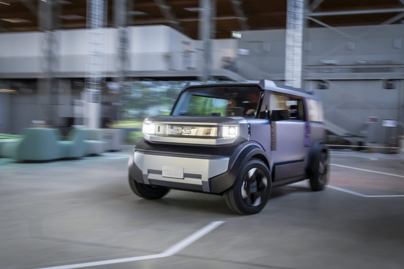 Dacia Hipster Elektrokonzept in Grau-Lila fährt durch eine Halle – markante Kastenform mit LED-Scheinwerfern