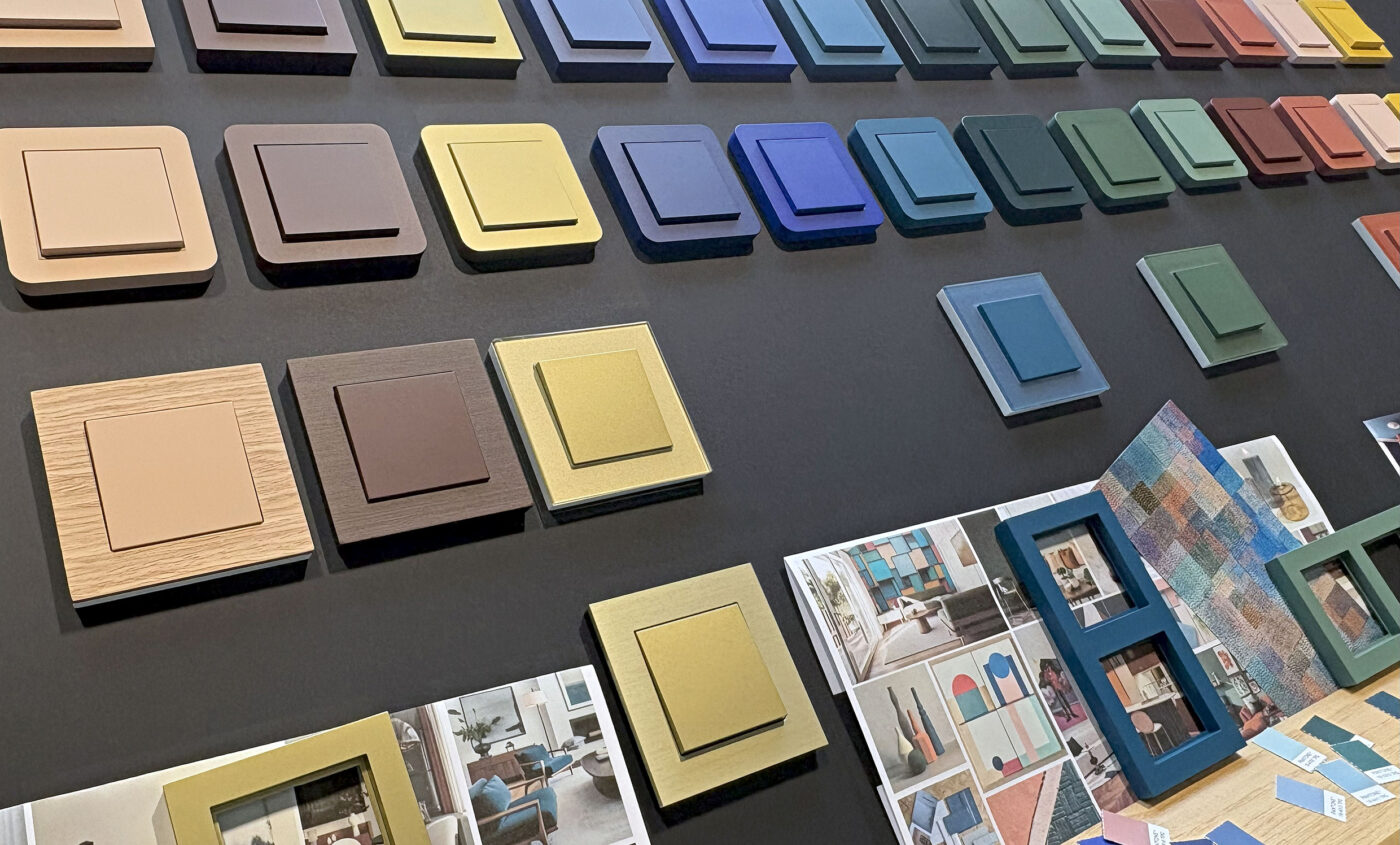 Hager Signature-Schaltersortiment in 16 Farben an dunkler Ausstellungswand, darunter Gold, Blau, Grün und Holzoptik