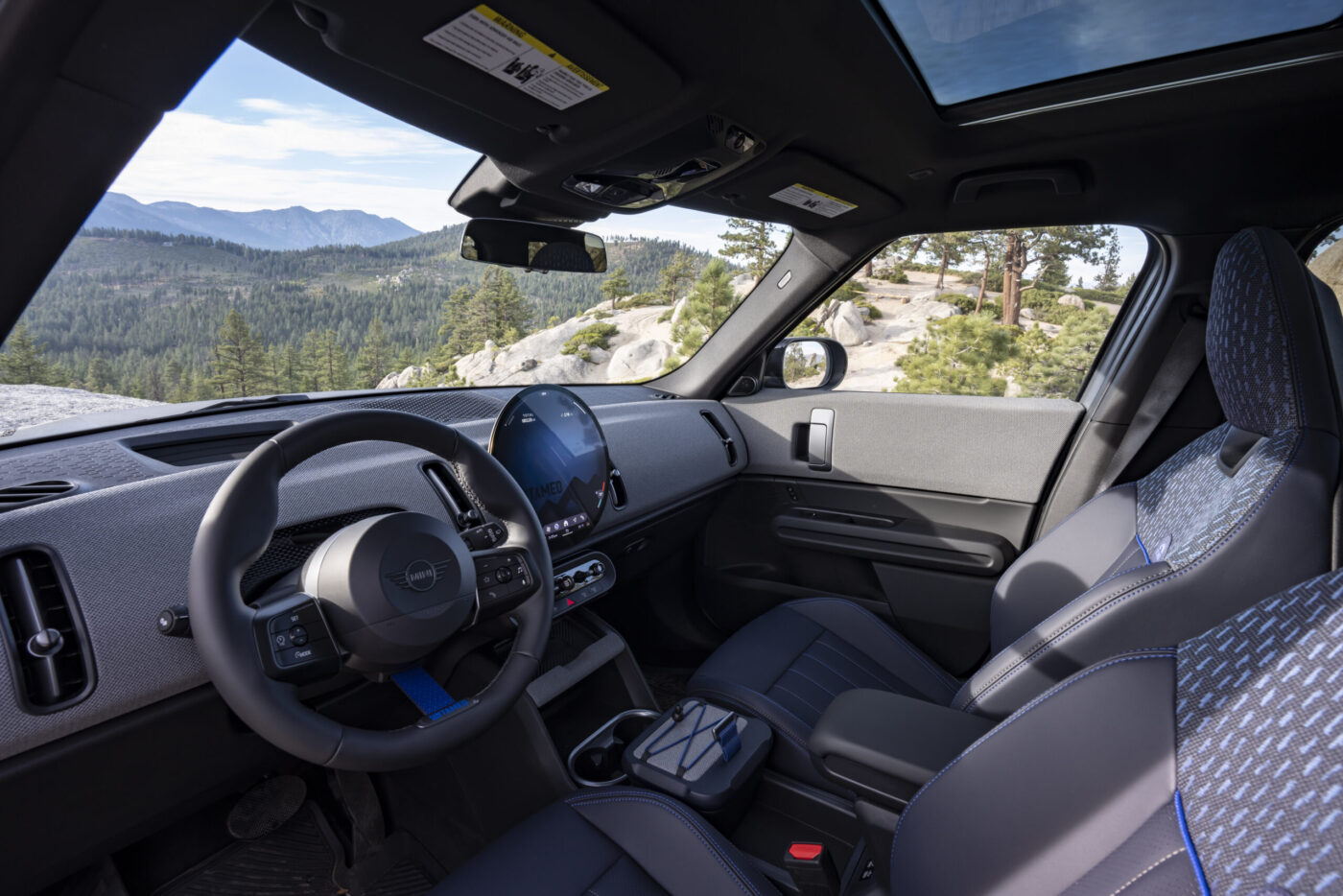 MINI Countryman Untamed Edition Cockpit mit Lenkrad, rundem Display und blau akzentuierten Sitzen vor Bergpanorama