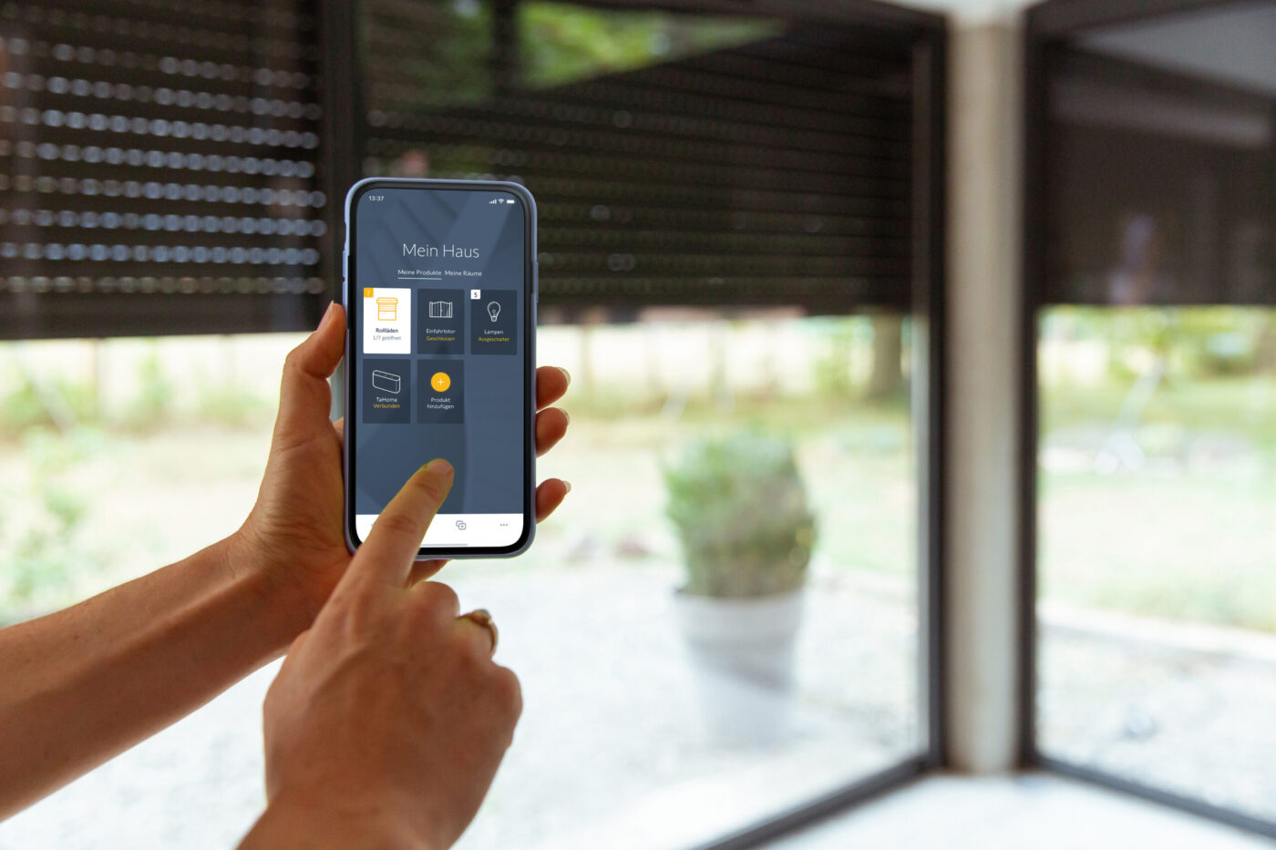 Hände bedienen TaHoma-App auf Smartphone zur Steuerung von Rollläden und Smart-Home-Geräten