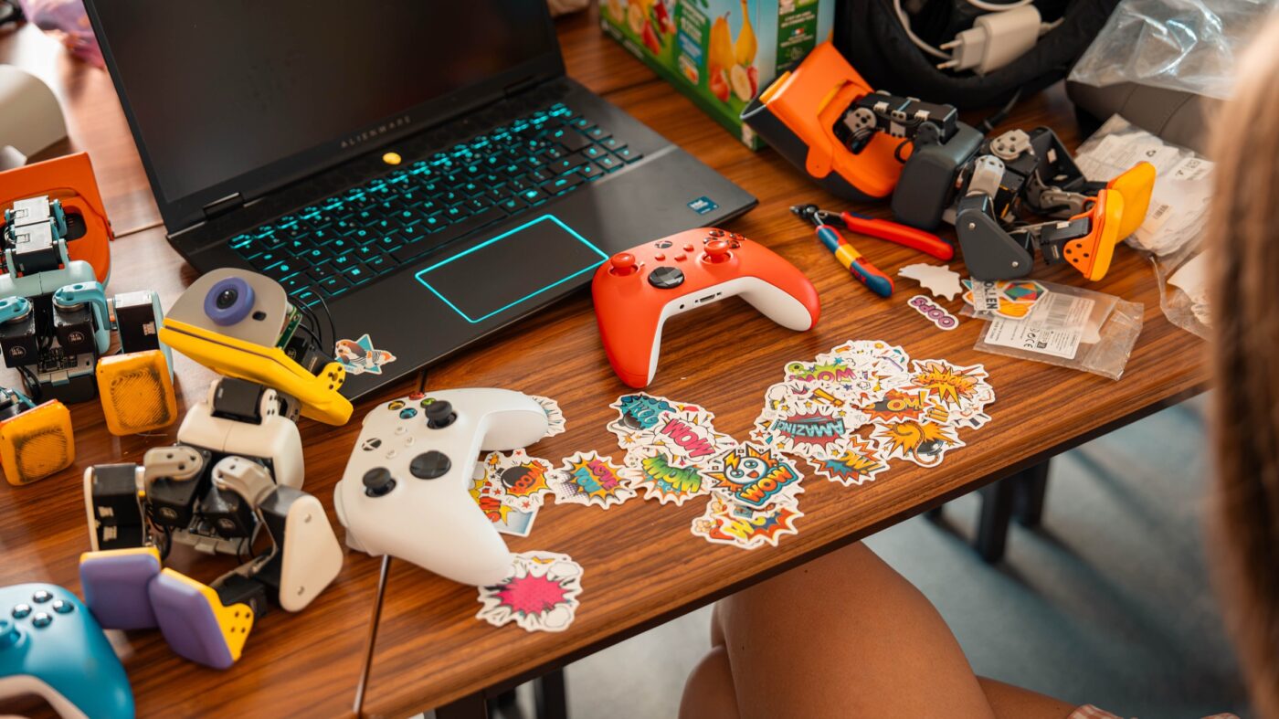 Mehrere Microduck-Roboter auf einem Schreibtisch mit Laptop, Gamecontrollern und Stickern