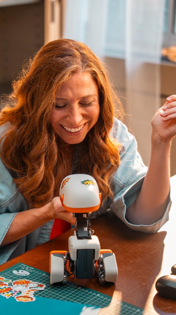 Lachende Frau mit einem weißen Microduck-Roboter auf einem Tisch