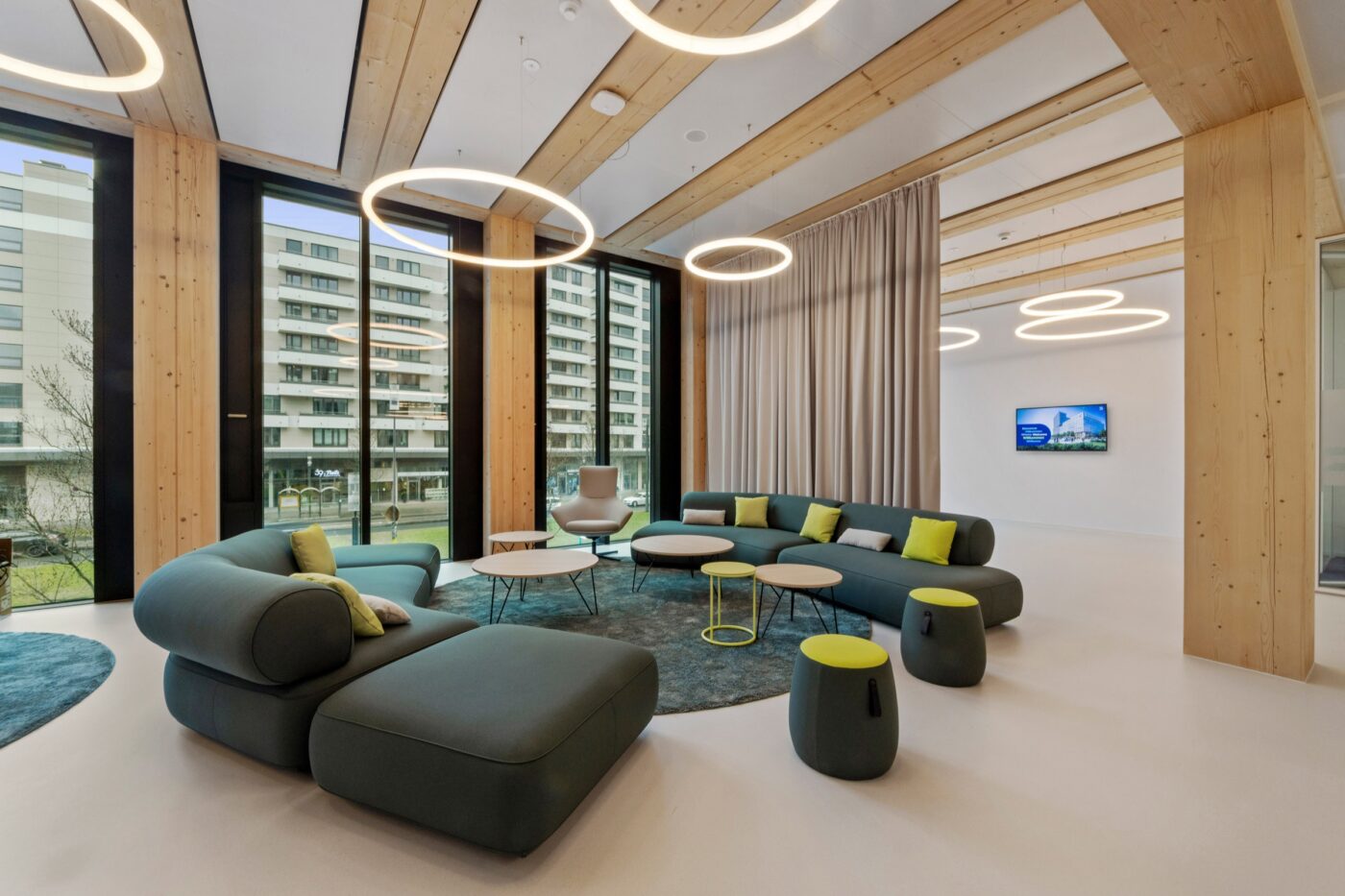 Lounge im Timber Pioneer mit grünen Sofas, Holzsäulen und runden Artemide-Leuchten an der Decke